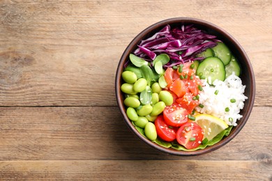 Photo of Poke bowl with salmon, edamame beans and vegetables on wooden table, top view. Space for text
