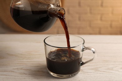 Photo of Pouring coffee into cup at light wooden table, closeup