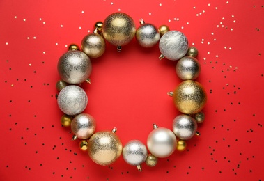 Photo of Beautiful festive wreath made of color Christmas balls on red background, top view