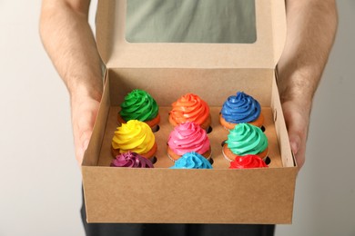 Photo of Man holding box with delicious colorful cupcakes on light background, closeup