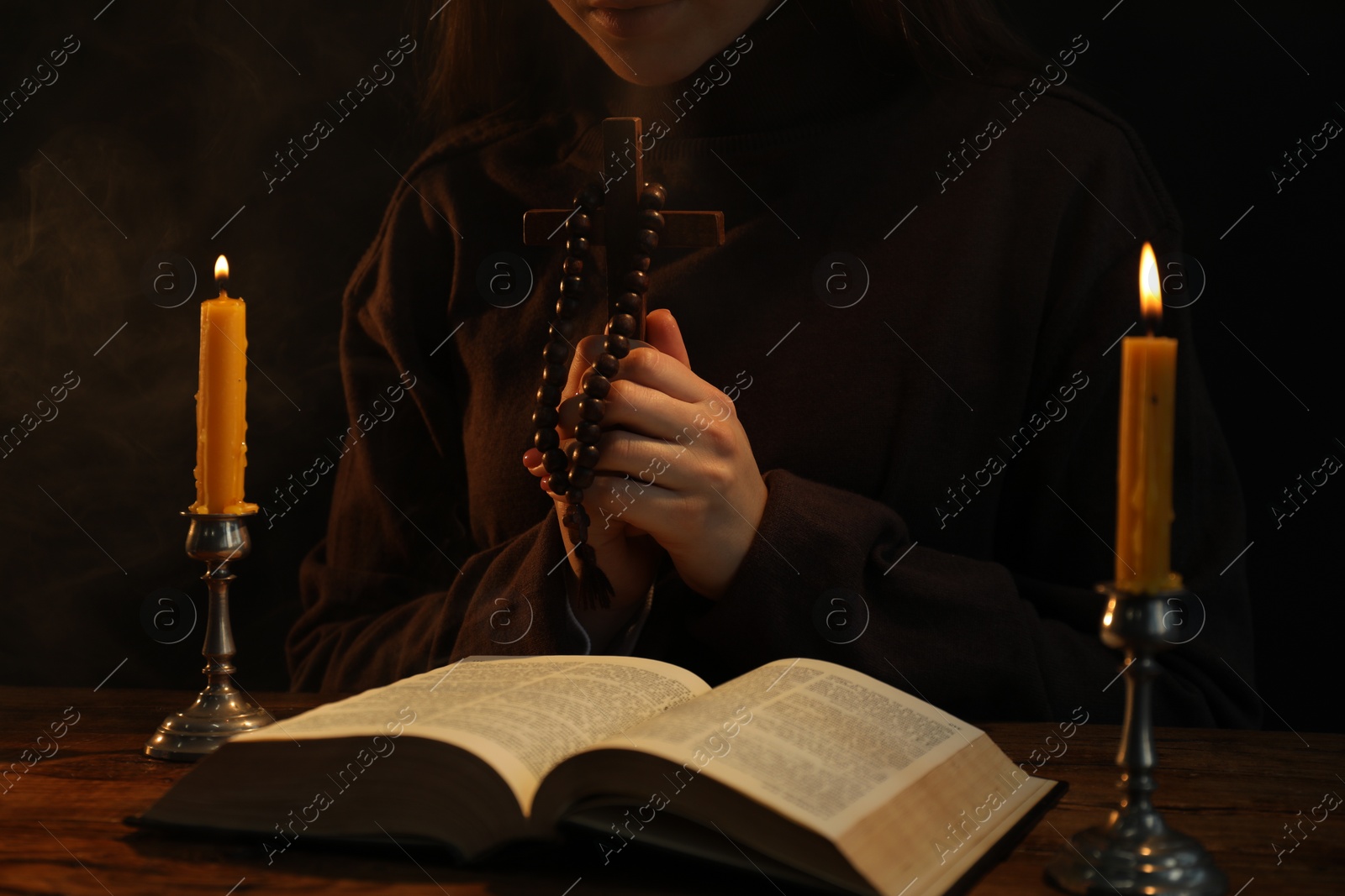 Photo of Woman praying at table with burning candles and Bible, closeup