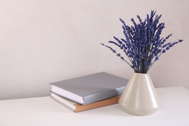 Photo of Bouquet of beautiful preserved lavender flowers and notebooks on white table near beige wall, space for text