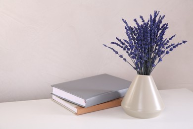 Bouquet of beautiful preserved lavender flowers and notebooks on white table near beige wall, space for text