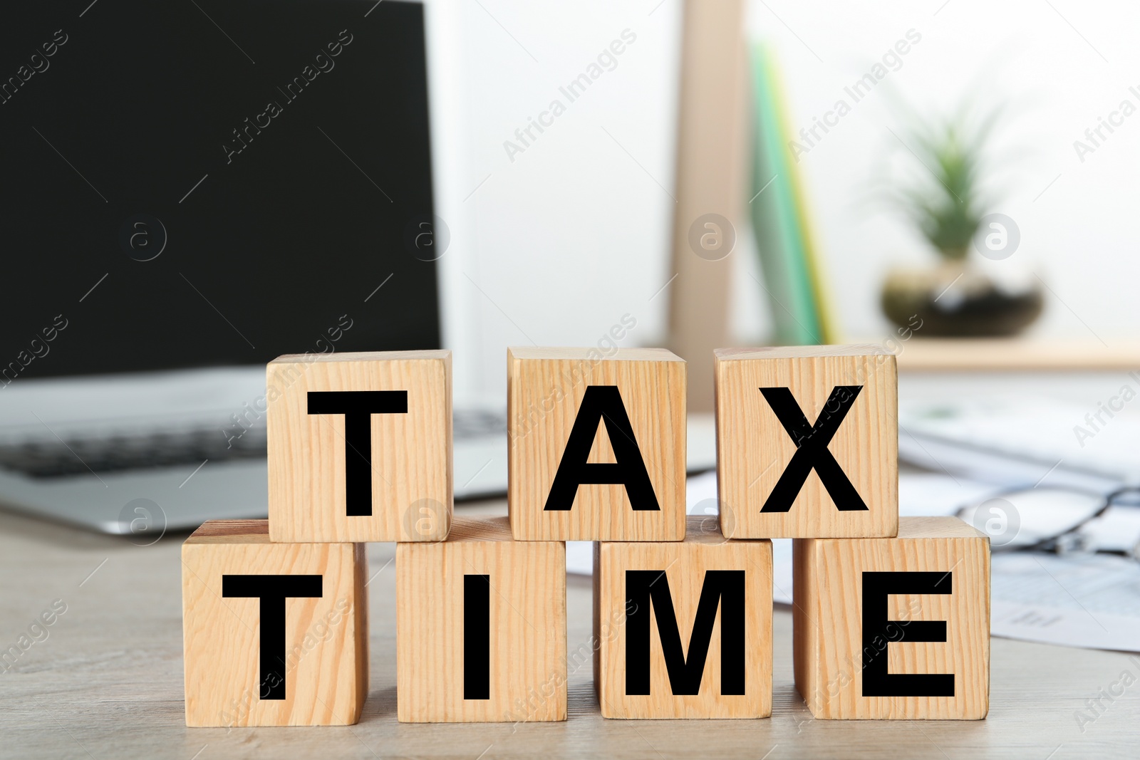 Photo of Wooden cubes with words Tax Time near laptop on table indoors