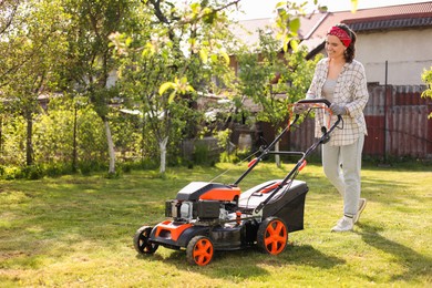 Photo of Smiling woman cutting green grass with lawn mower in garden