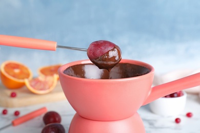 Photo of Dipping grape into pot with chocolate fondue on table, closeup