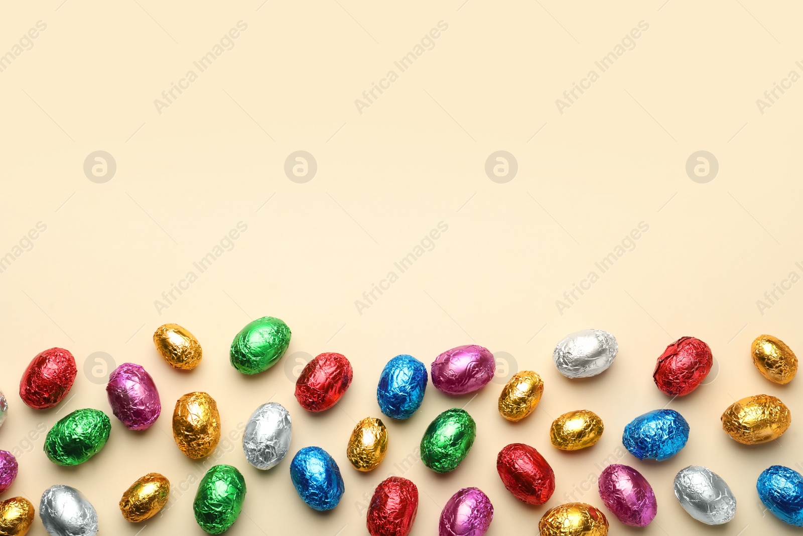 Photo of Chocolate eggs wrapped in colorful foil on beige background, flat lay. Space for text