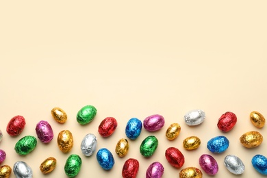 Chocolate eggs wrapped in colorful foil on beige background, flat lay. Space for text