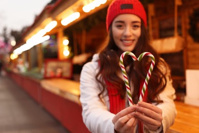 Photo of Young woman spending time at Christmas fair, focus on candy canes. Space for text