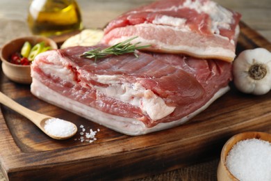 Pieces of raw pork belly, salt, oil, garlic and rosemary on wooden table, closeup