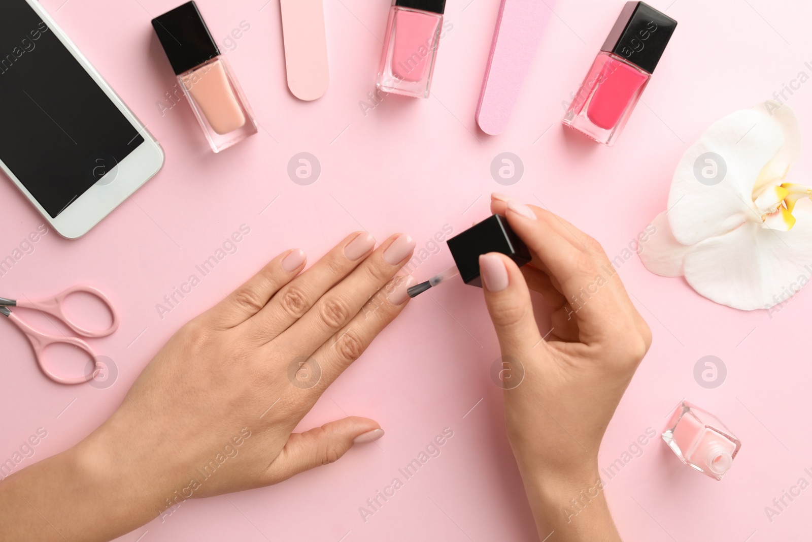 Photo of Woman applying nail polish on color background, top view