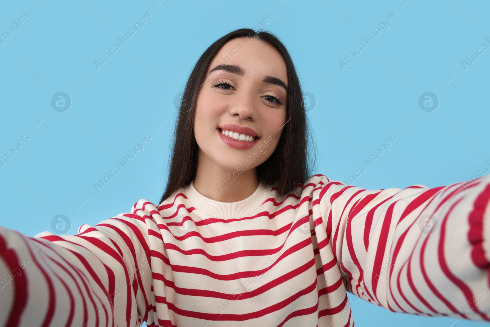 Photo of Smiling young woman taking selfie on light blue background