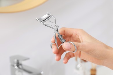 Photo of Woman with eyelash curler in bathroom, closeup. Space for text