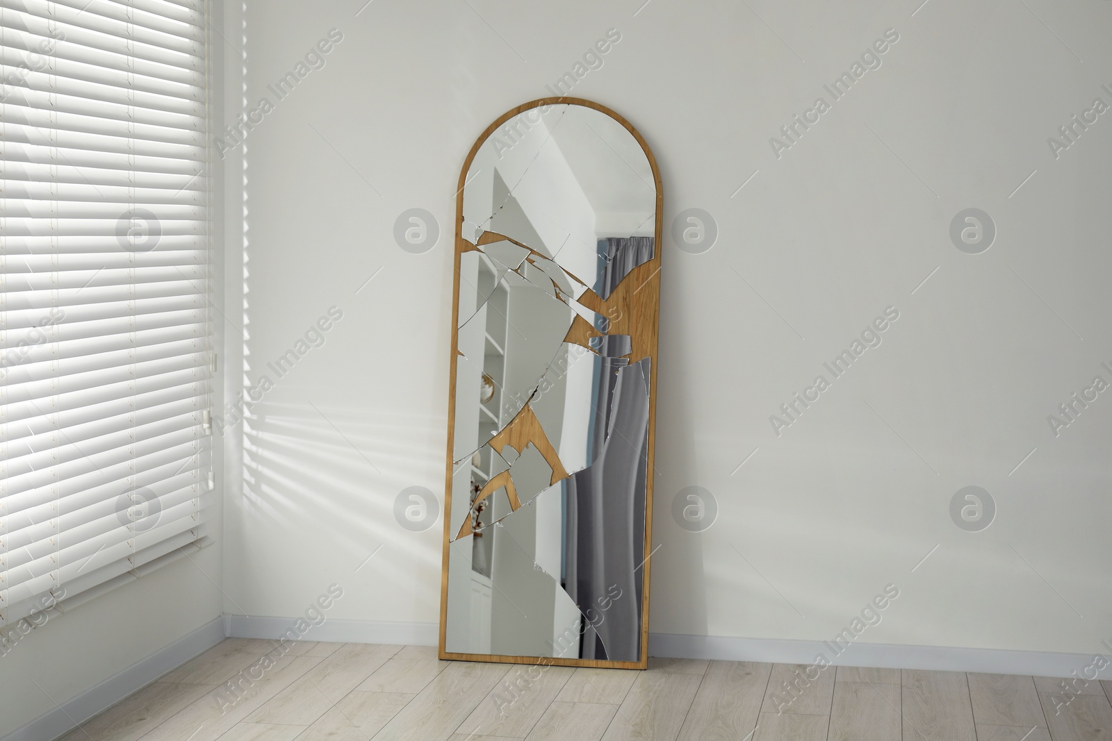 Photo of Broken mirror with many cracks near white wall indoors