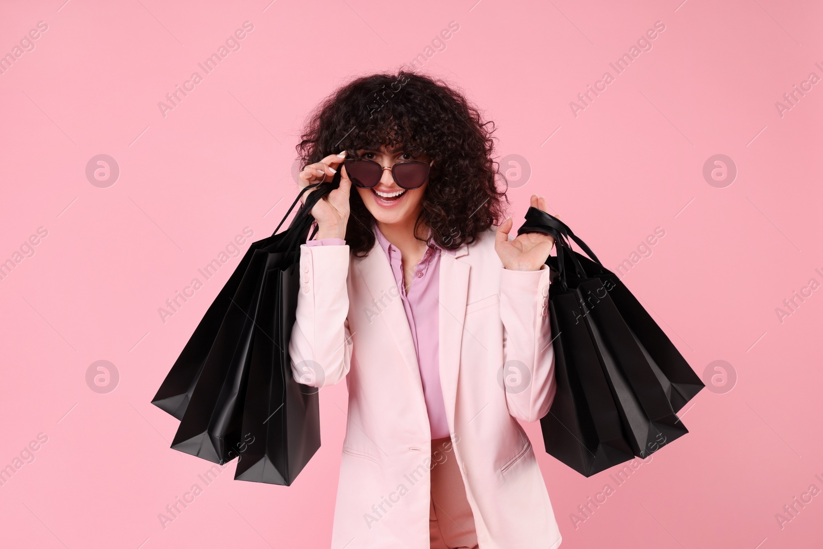 Photo of Happy young woman with shopping bags and stylish sunglasses on pink background