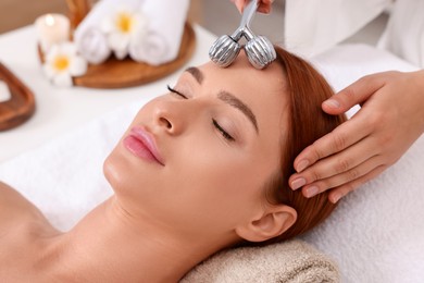 Young woman receiving facial massage with metal roller in beauty salon, closeup