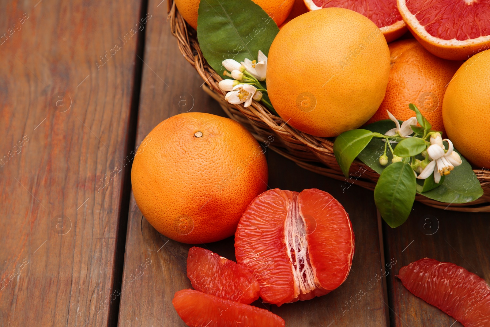 Photo of Wicker basket with fresh grapefruits and green leaves on wooden table