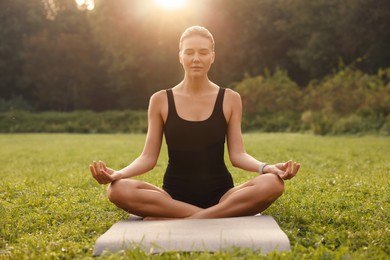 Beautiful woman practicing yoga on mat outdoors. Lotus pose