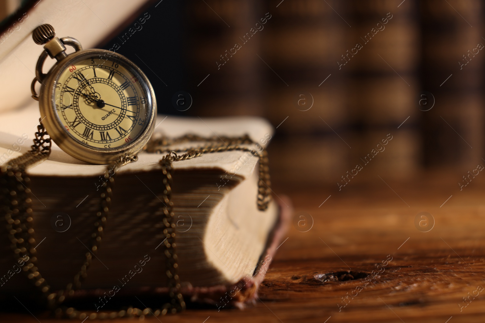 Photo of Pocket clock with chain and book on wooden table, closeup. Space for text