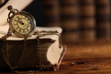 Pocket clock with chain and book on wooden table, closeup. Space for text