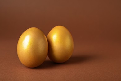 Photo of Shiny golden eggs on brown background, closeup. Space for text