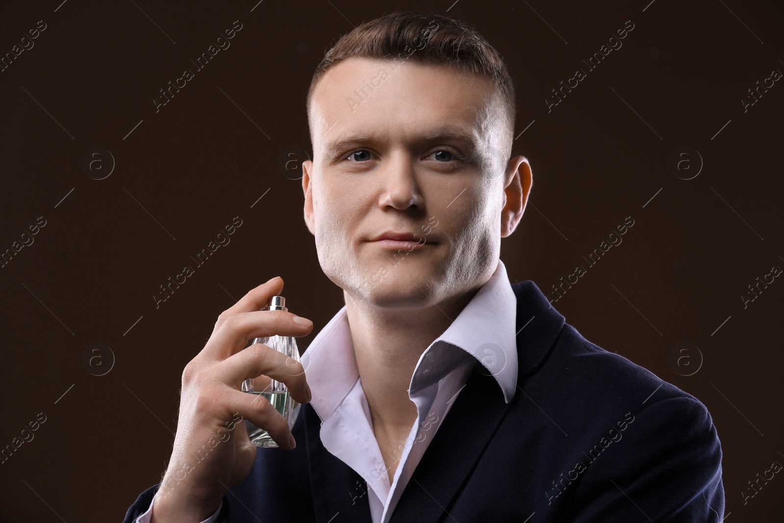 Photo of Handsome man in suit using perfume on dark background