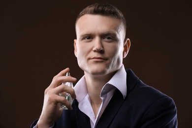 Handsome man in suit using perfume on dark background