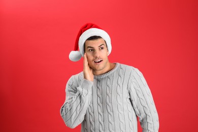 Photo of Surprised man wearing Santa hat on red background