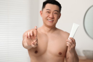 Photo of Handsome man with tube of body cream indoors, selective focus