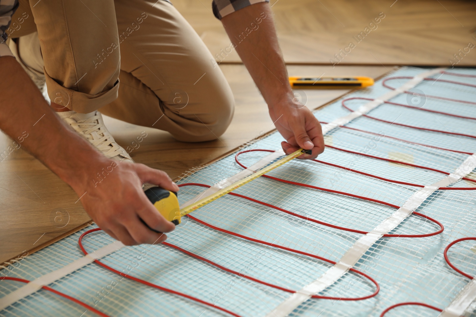 Photo of Professional worker installing electric underfloor heating system indoors, closeup