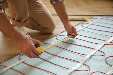 Professional worker installing electric underfloor heating system indoors, closeup