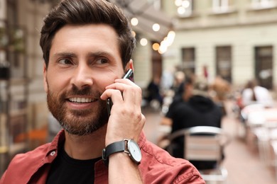 Photo of Handsome man talking on smartphone while walking outdoors, space for text