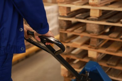 Image of Worker moving wooden pallets with manual forklift in warehouse, closeup