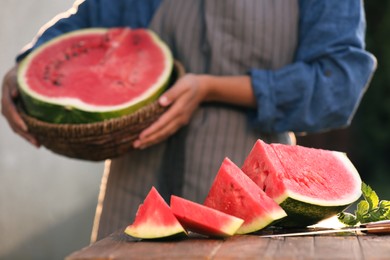 Photo of Woman holding wicker basket outdoors, closeup. Focus on delicious ripe watermelon slices with mint