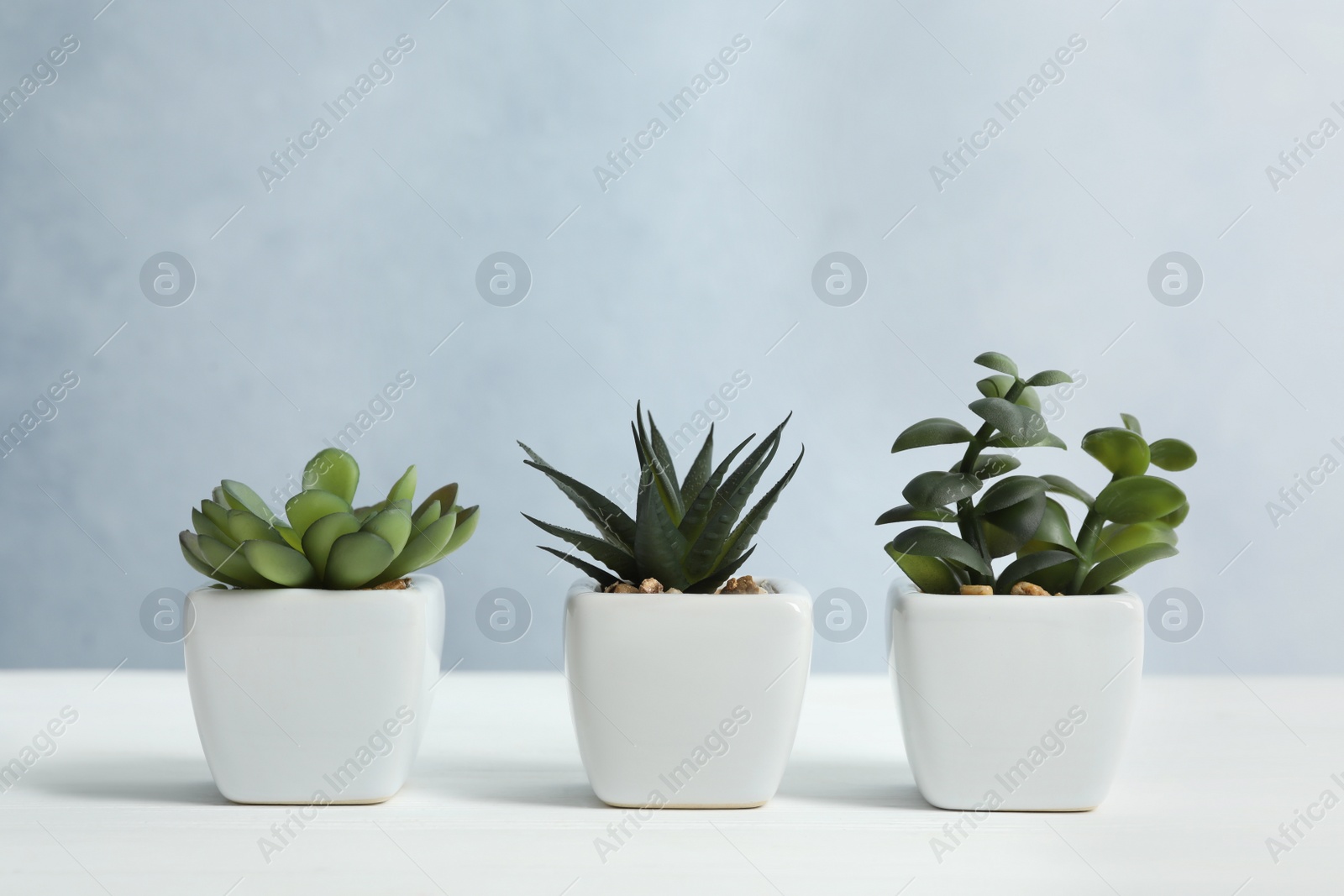 Photo of Artificial plants in flower pots on white wooden table