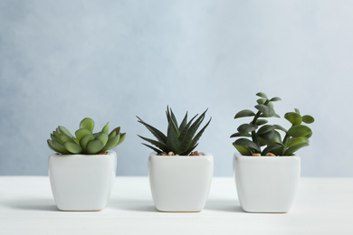 Artificial plants in flower pots on white wooden table