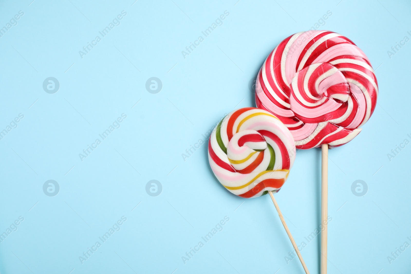 Photo of Sticks with colorful lollipops on light blue background, flat lay. Space for text