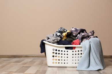 Photo of Laundry basket with dirty clothes on floor indoors. Space for text
