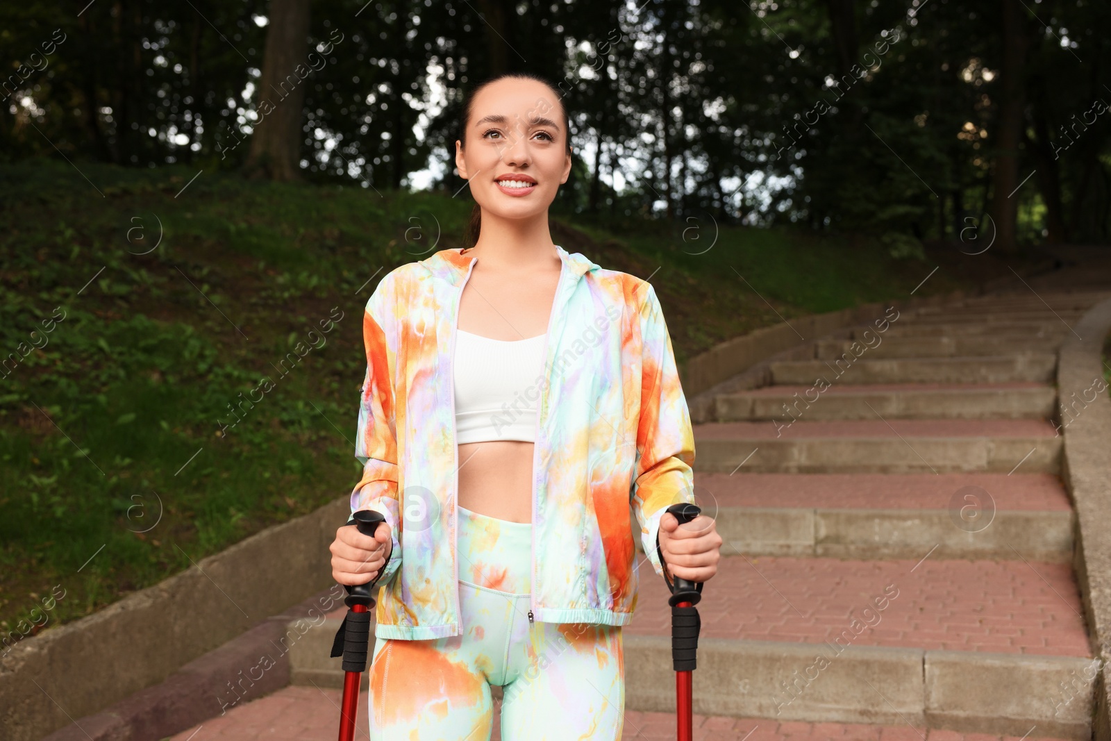 Photo of Young woman practicing Nordic walking with poles on steps outdoors