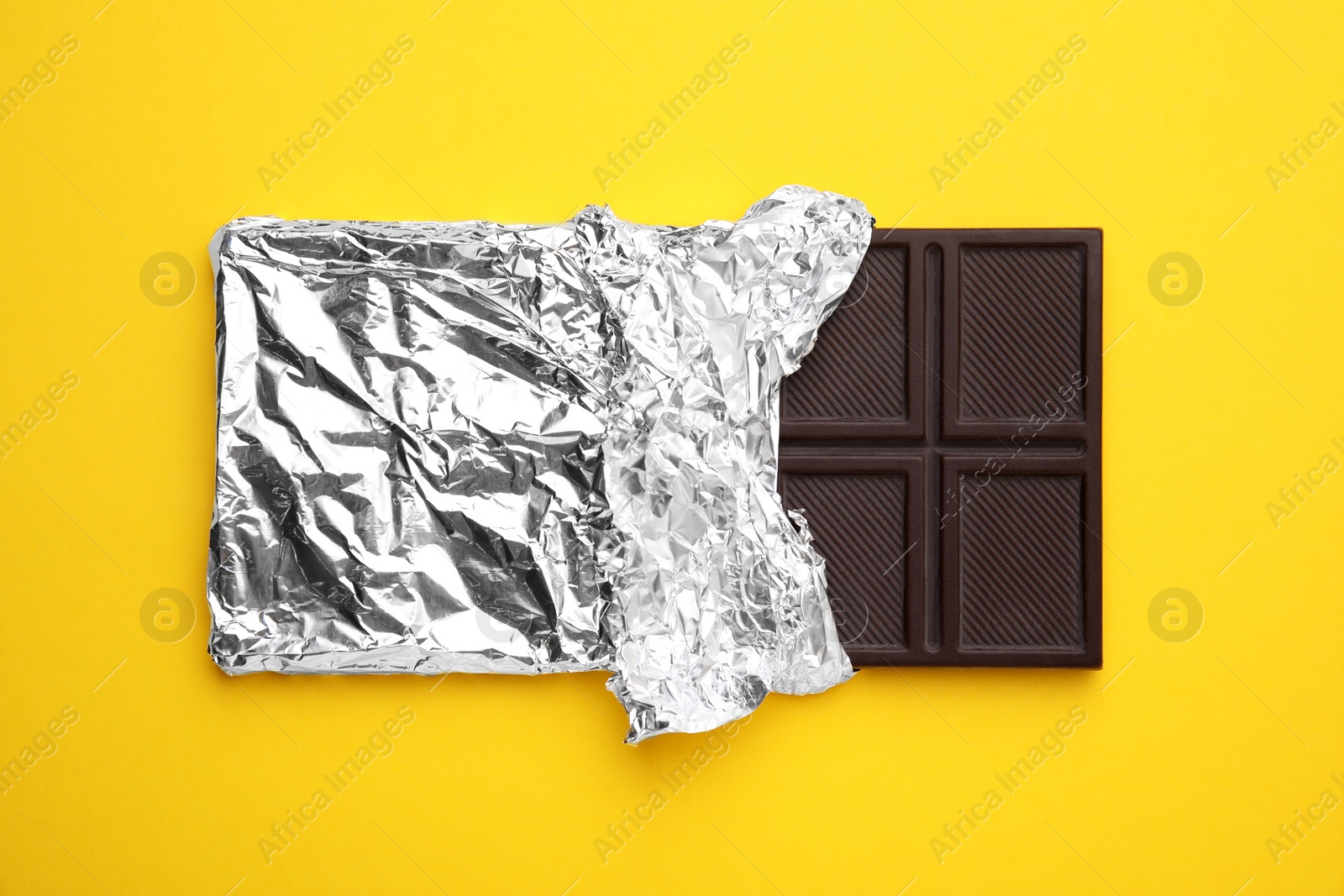 Photo of Tasty chocolate bar on yellow background, top view