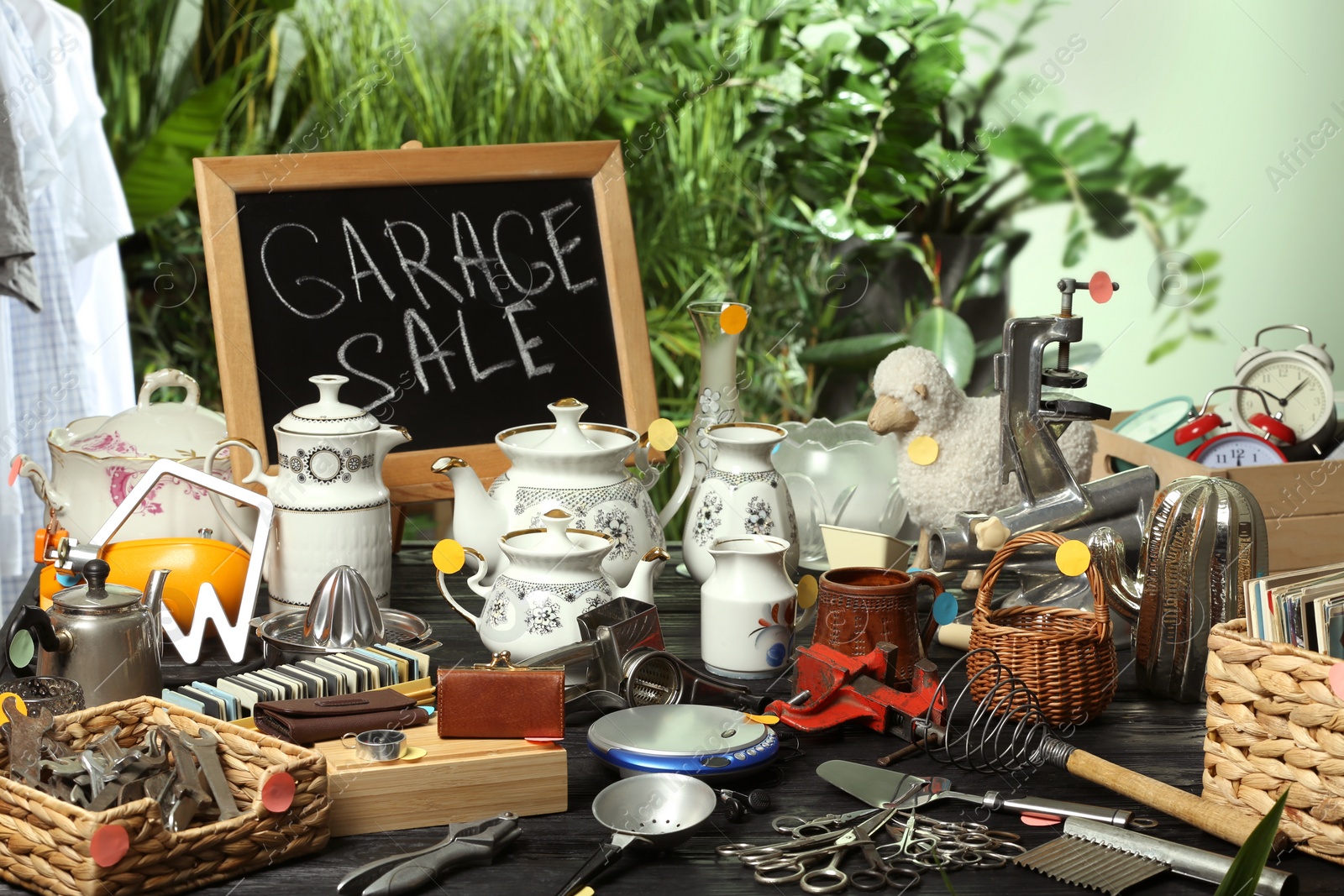 Photo of Blackboard with sign Garage Sale and many different stuff on black wooden table indoors