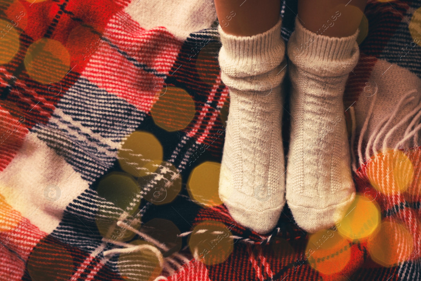 Image of Woman in knitted socks on warm plaid, top view. Space for text