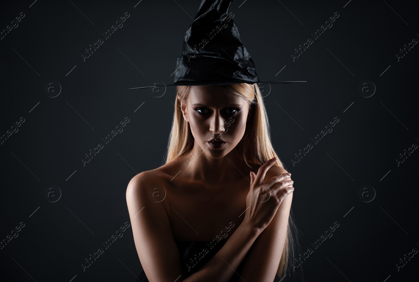 Photo of Witch in black hat on dark background. Scary fantasy character