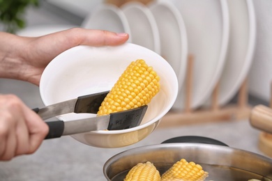 Photo of Woman putting raw corn cob into stewpot, closeup