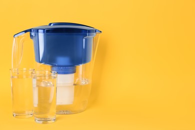 Photo of Filter jug and glasses with purified water on yellow background. Space for text