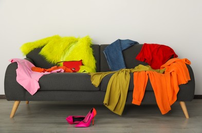 Messy pile of colorful clothes on sofa and shoes in living room