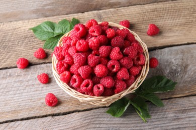 Wicker basket with tasty ripe raspberries and green leaves on wooden table