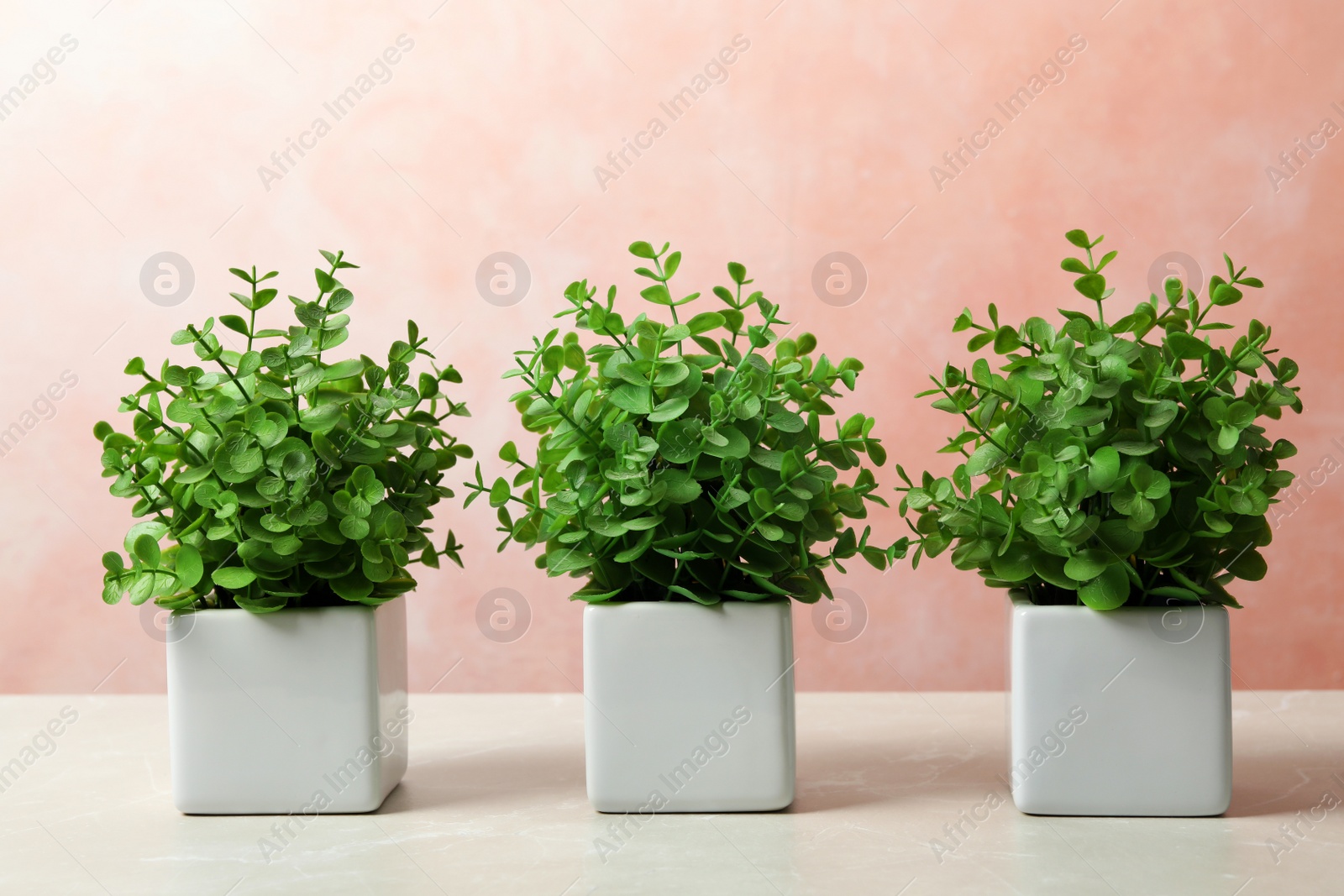 Photo of Beautiful artificial plants in flower pots on light marble table against color background