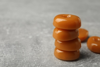 Photo of Stacked tasty hard toffee candies on light grey table, closeup. Space for text