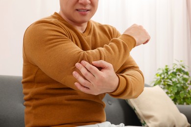 Photo of Man suffering from pain in his elbow on sofa indoors, closeup